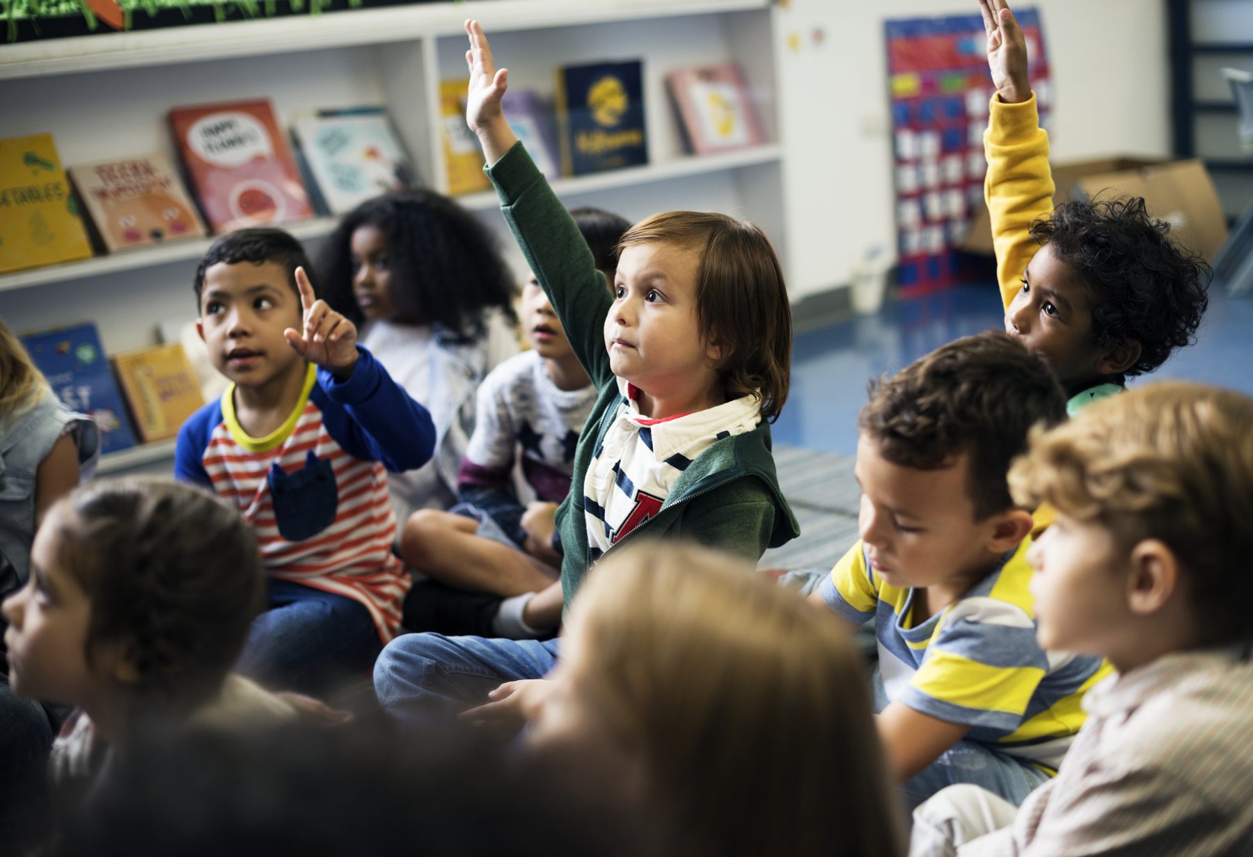 Children sitting together in a bright classroom with their hands raised