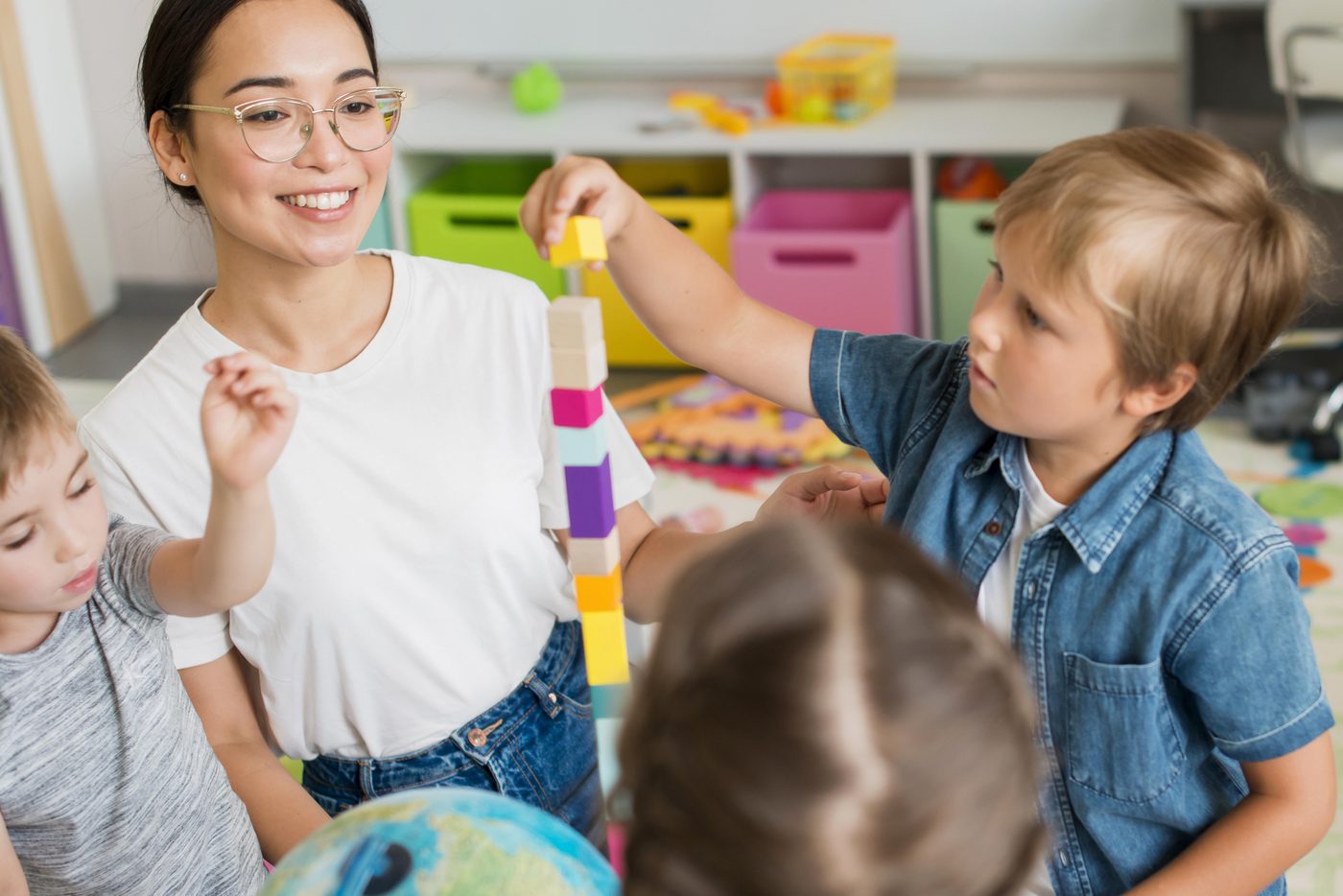 A teacher helping toddlers stack a colorful tower